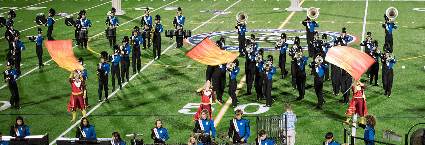 The band performs at a competition, the guard is waving flags.